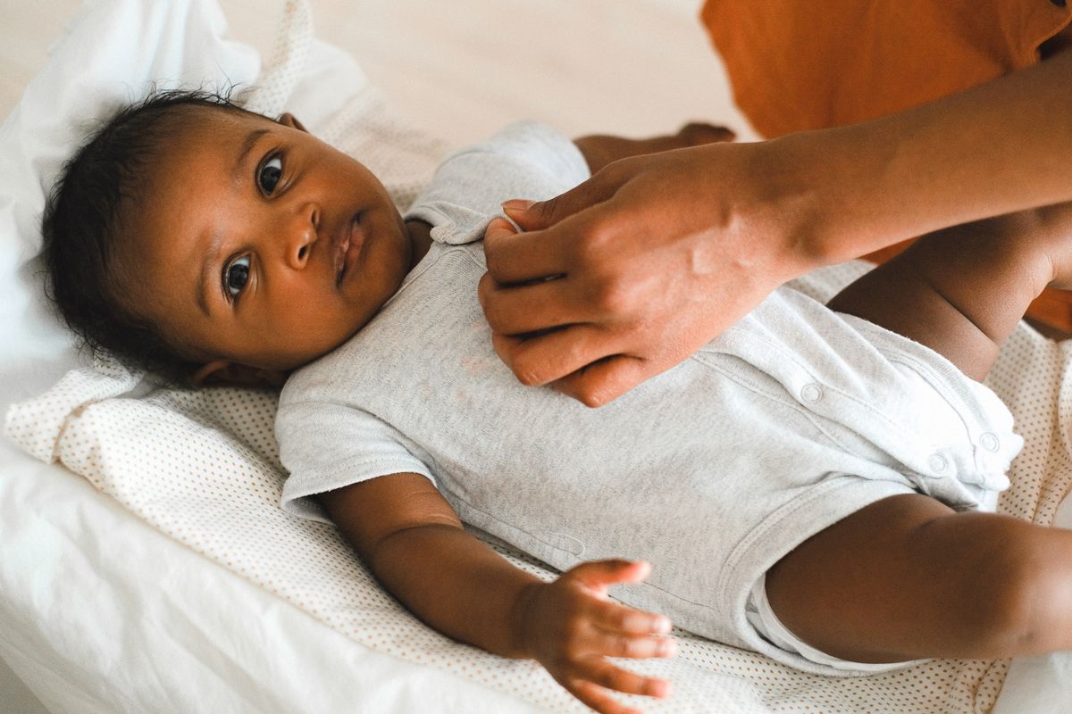 Una madre cambia la ropa a su bebé, que la mira tumbado