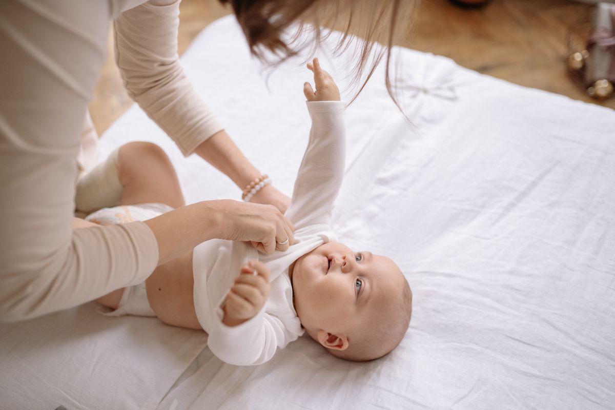 Una madre viste a su bebé sobre la cama